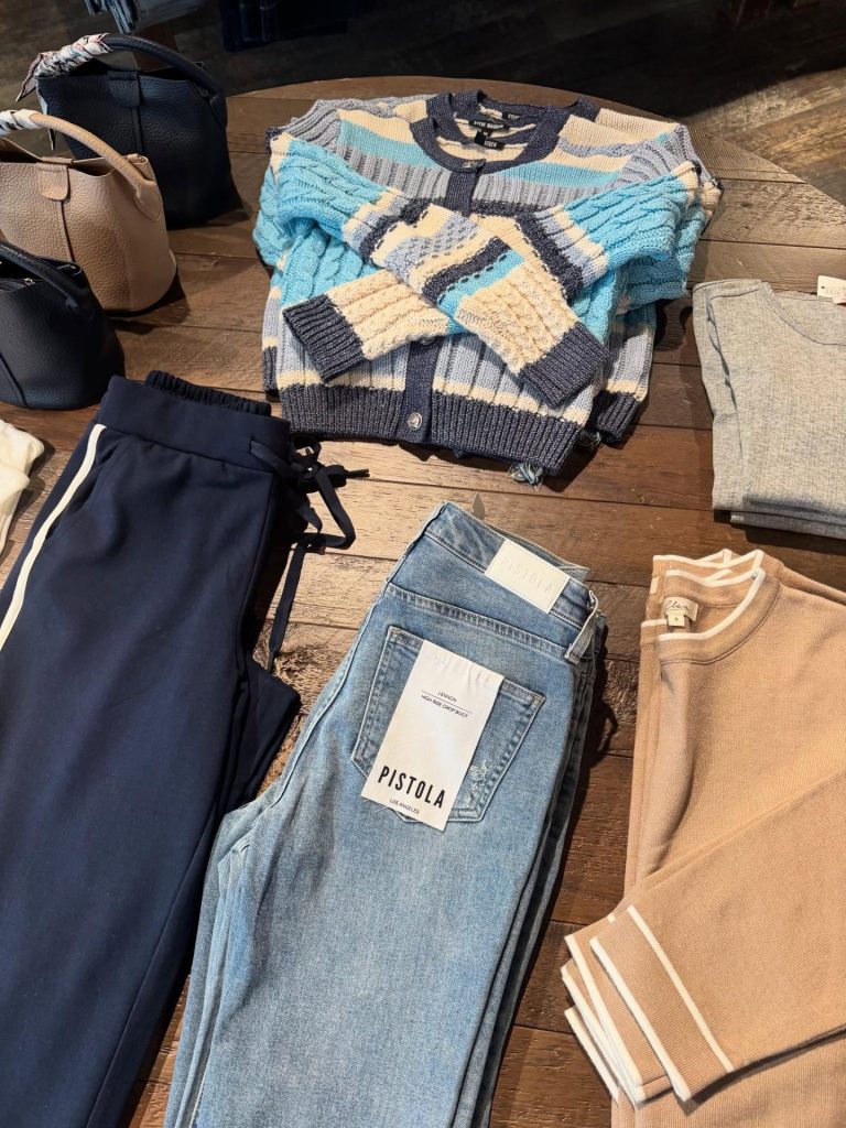 table of clothing at deerfield boutique with sweather, jeans, pants, purses, etc.